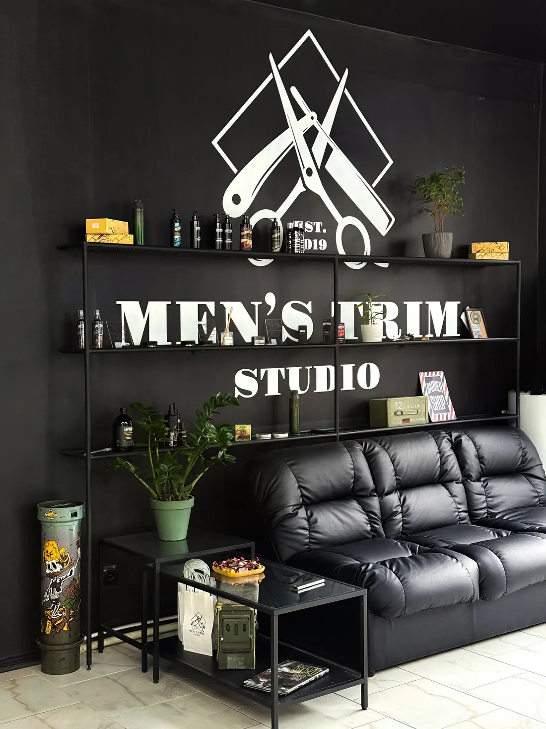 Men's Trim Studio interior: logo wall, shelves with grooming products, leather sofa